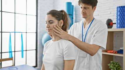 A male physiotherapist examines the neck of a female patient in a modern rehabilitation clinic.