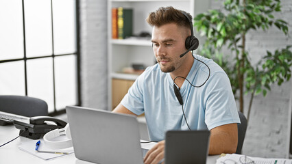 Handsome young hispanic man in a headset working indoors at his computer in a modern office.