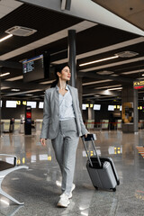 Asian woman with luggage is walking in airport terminal. Girl tourist with a suitcase and tickets...