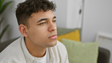 A thoughtful young man with curly hair rests at home, showcasing contemplation and casual style.
