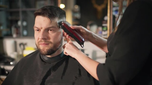 Young female barber making men's undercut haircut hairstyle using Haircut Clipper in Modern style barber shop. Haircare service local small business, cosmetics and personal care industry 4K video