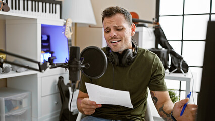 A hispanic man sings indoors while recording in a professional music studio, with a microphone and...