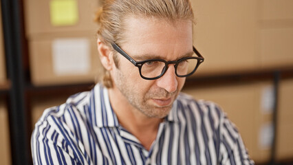 Focused man with glasses and ponytail wearing striped shirt working in a warehouse office setting