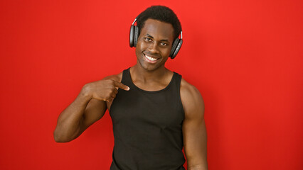 Smiling young african american man with headphones pointing at himself against a red background.