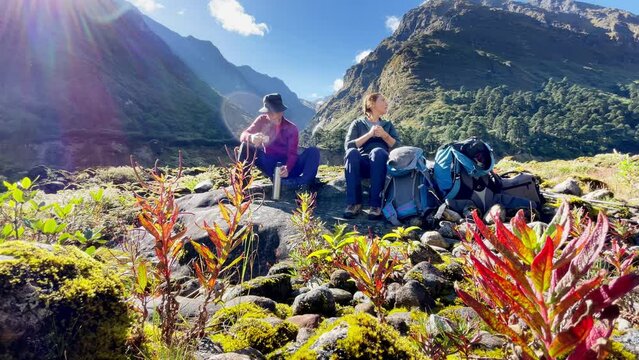 4K footage of Young Couple sitting on stones, resting, drinking tea in Makalu Barun National Park on Mera peak climbing route. They left Backpacks and trekking poles and enjoying valley sunny day view