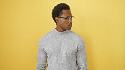 A contemplative young adult black man with glasses against a yellow isolated background