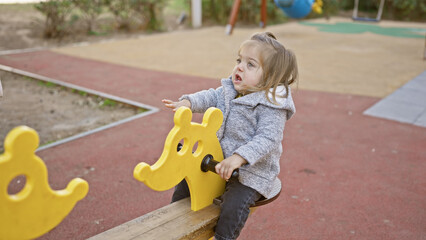Adorable blonde girl playing on a yellow seesaw in a playground, capturing a moment of childhood...