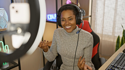Smiling woman with headphones in a gaming room using microphone and ring light indoors at home