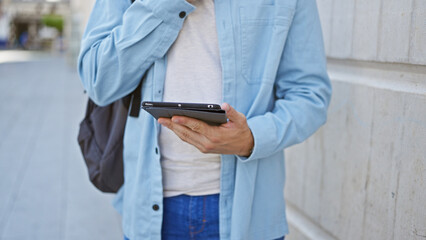 Hispanic man using tablet on urban street, dressed in light blue jacket, technology outdoors.