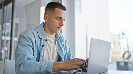 Handsome young hispanic man studying on a laptop indoors at a university campus, exemplifying modern education.