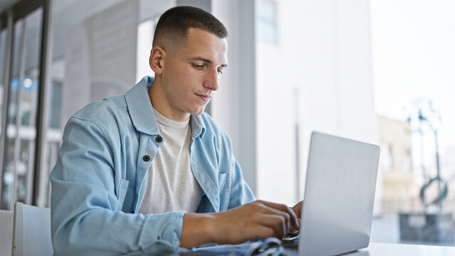 Handsome young hispanic man studying on a laptop indoors at a university campus, exemplifying modern education.