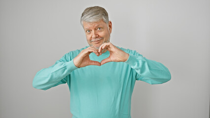 Smiling senior man forming heart shape with hands against white background expresses love and...