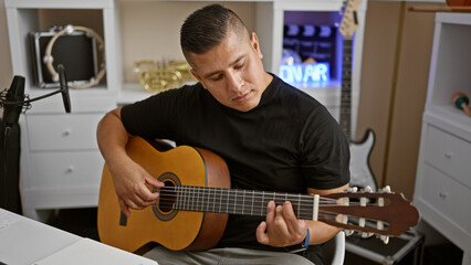 Obraz premium Handsome young latin man immerses soul into playing classical guitar, creating melody magic within club's intimate music studio ambiance