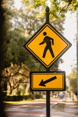 Yellow Pedestrian crossing sign with arrow pointing to the road with tree canopy in background verticle