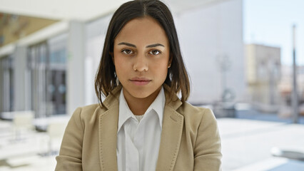 Portrait of a confident young hispanic woman dressed in business attire against a blurred urban...