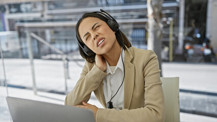 Annoyed young woman wearing headphones experiencing discomfort at office with blurred background