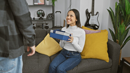 Woman receiving a gift from a man in a cozy living room, expressing joy and love together in an...