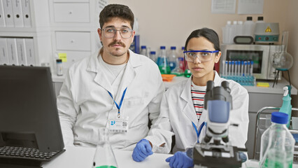 Woman and man scientists working together in a laboratory, surrounded by scientific equipment and computers.