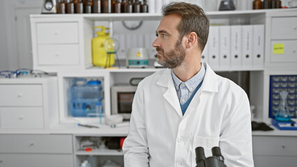 Bearded man in labcoat standing thoughtfully in a modern laboratory, portraying medical...