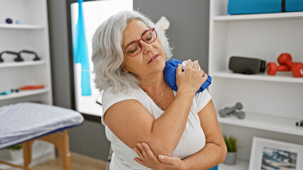 Mature woman in clinic holding ice pack on shoulder in pain