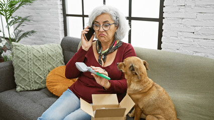 Grey-haired woman in conversation on phone, examining a dog comb indoors with concerned expression,...