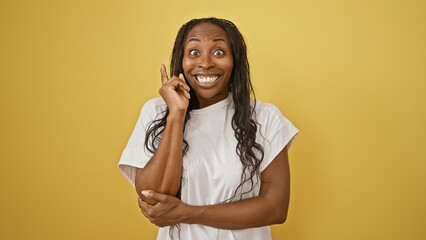 A cheerful young woman with curly hair wears a white shirt, standing against a yellow background,...