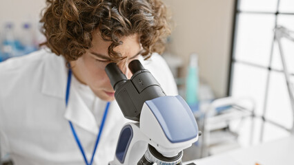 Young hispanic male scientist examining samples with a microscope in a bright laboratory setting.