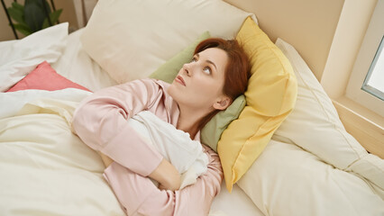 A contemplative young woman lies in a bedroom with colorful pillows, exuding calmness and comfort.