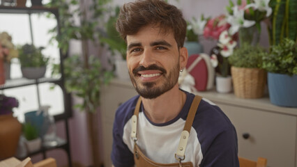Handsome hispanic man working in a vibrant indoor flower shop smiling at the camera.
