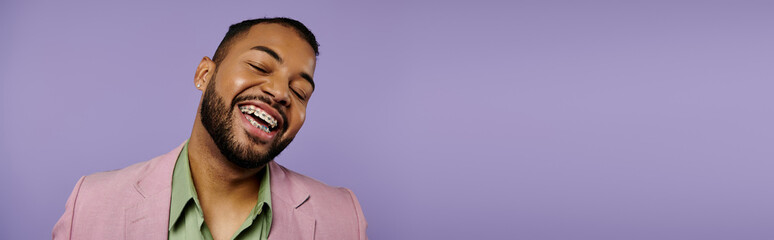 Young African American man with braces laughing joyfully in a stylish pink jacket against a vibrant...