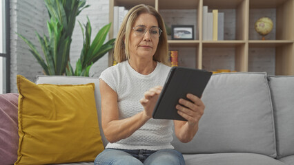 Obraz premium Mature woman reading tablet on sofa in a cozy living room