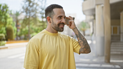 Handsome hispanic man with beard and tattoos smiling outside in an urban city setting.