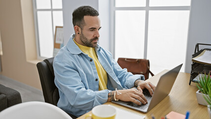 A professional young man with a beard working on a laptop in a modern office setting.