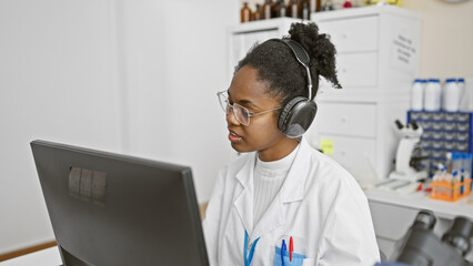 African american woman wearing headphones working intently at a computer in a laboratory setting.