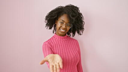 A welcoming african american woman with glasses and curly hair in a pink sweater against a plain...