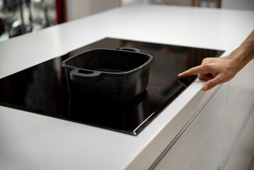 Man hand turns on black induction cooker with sausepan