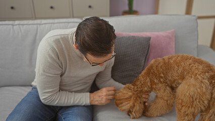 A middle-aged man pets a poodle in the cozy living room of a modern apartment.