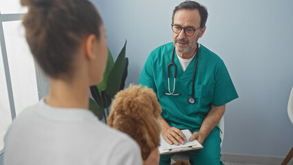 Hispanic veterinarian man consults with a woman about her poodle in a clinic room, showcasing a...