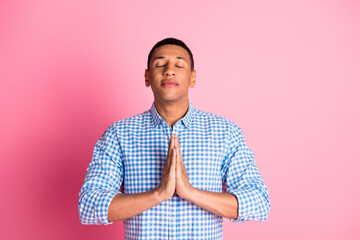 Photo of handsome dreamy guy wear plaid shirt arms together praying emtpy space isolated pink color...