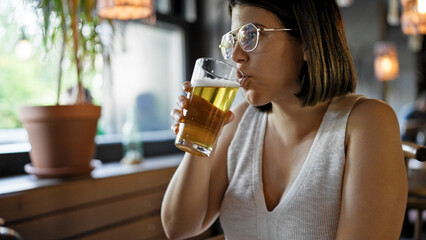 Young beautiful hispanic woman drinking beer at the restaurant