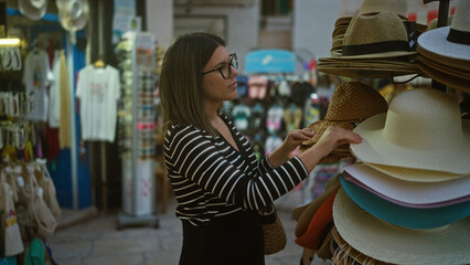 A young hispanic woman shopping for hats in the charming streets of polignano a mare, puglia,...