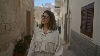 Young, beautiful hispanic woman smiling and walking through charming, narrow streets of polignano a...