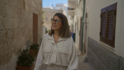 Fototapeta premium Young, beautiful hispanic woman smiling and walking through charming, narrow streets of polignano a mare, puglia, italy, showing historic architecture and european ambiance.