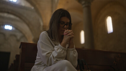 A young hispanic woman is praying in a historic christian church in italy, surrounded by beautiful...