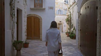 A young, hispanic woman walks down the charming streets of polignano a mare, puglia, italy,...