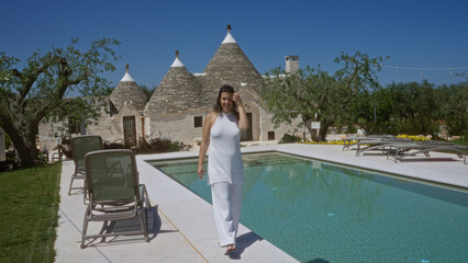 Beautiful young woman walking by a pool in alberobello, italy, with traditional trulli houses in...