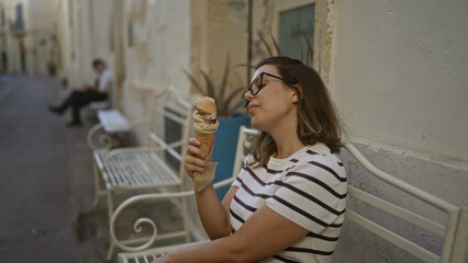 Young woman enjoying an ice cream cone while sitting on a bench in the charming streets of lecce,...
