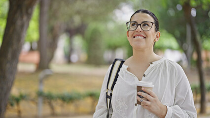 Young beautiful hispanic woman smiling drinking take away coffee at the park