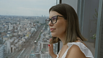 Beautiful young hispanic woman wearing glasses looking though the window on skyscraper in japan
