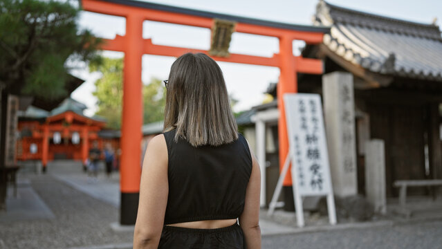 Beautiful brunette hispanic woman in glasses, walking away on a casual walk at fushimi inari-taisha, japan's sacred kyoto shrine, a heart-stirring view of her back